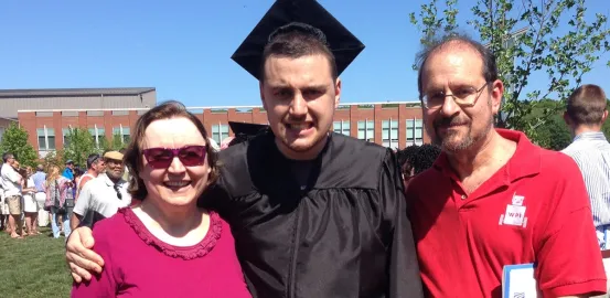 Ian H. wearing his cap and gown at graduation with his parents
