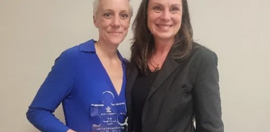 Iowa Medicaid Director Elizabeth Matney holding clear puzzle piece award and standing next to Autism Speaks representative
