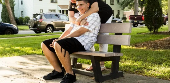 grandmother hugging young adult boy on an outside bench
