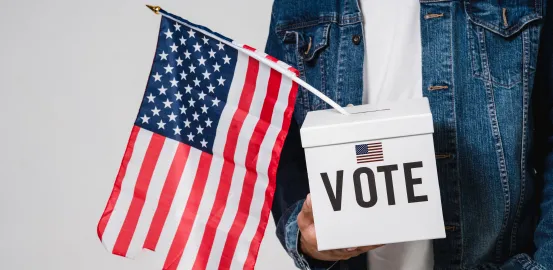 person holding a white box with "VOTE" on the front and an American flag hanging out the top