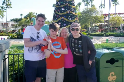 Kim McKafferty and her husband and son at Disney Land with a Christmas tree in the background.