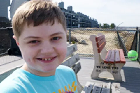 Kimberlee Rutan McCafferty's son sitting on a bench wearing a blue shirt 
