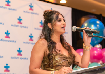 A woman wearing a gold dress speaking at an Autism Speaks event