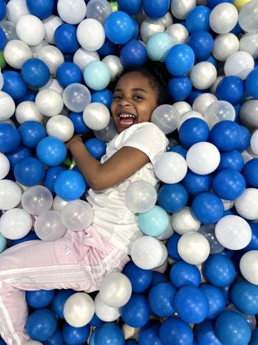 A young girl laughing while laying in a ball pit filled with blue and white balls