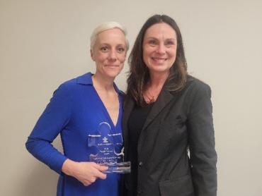 Iowa Medicaid Director Elizabeth Matney holding clear puzzle piece award and standing next to Autism Speaks representative