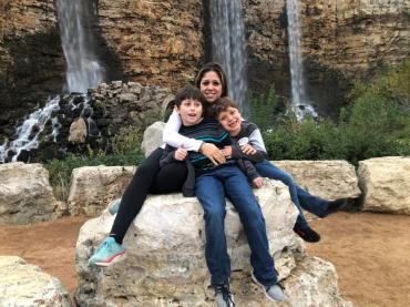 Susy and 2 of her children sitting on a big rock in front of a waterfall