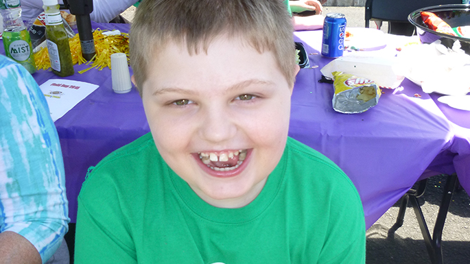 a little boy in a green shirt sitting at a picnic table and smiling