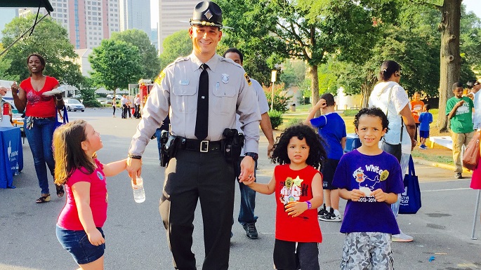 Photo of a first responder holding hands with children at a safety fair