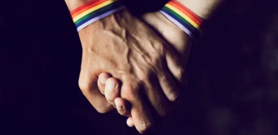 2 people holding hands with Pride bracelets on