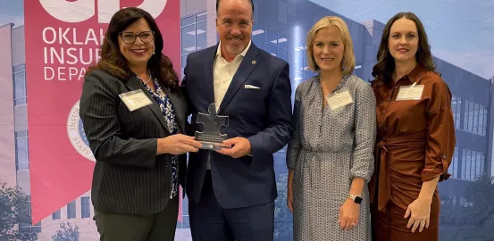 Christa Stevens handing Commissioner Mulready an puzzle shaped award with Judith Ursitti and Tara Hood standing next to them