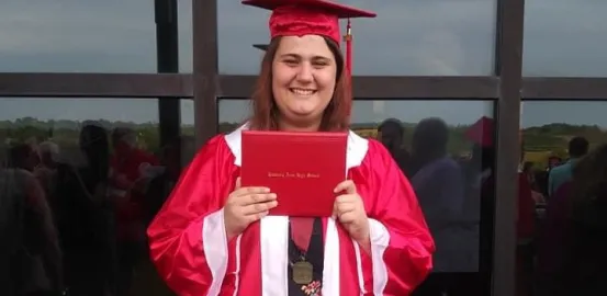 A woman holding a diploma and wearing a red graduation cap and gown