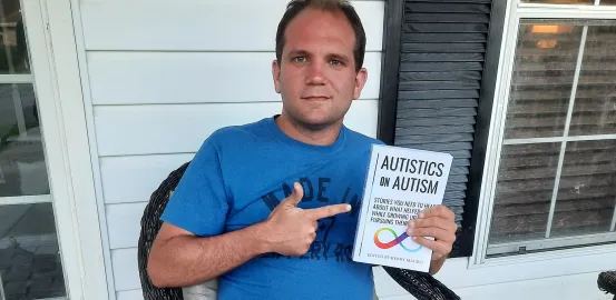 Josh holding a copy of the book "Autistics on Autism"