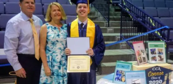 Connor posing in his. graduation gown and degree next to his mom and dad