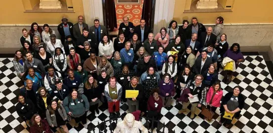 Large group of advocates standing on a black and white checkered floor in the capitol atrium