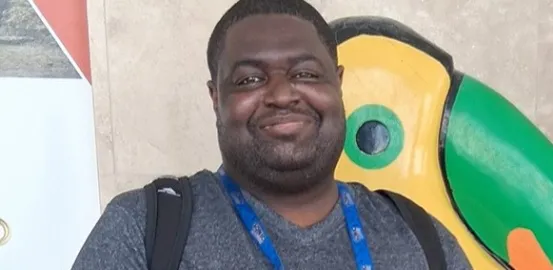 Man standing by a colorful toucan statue, smiling