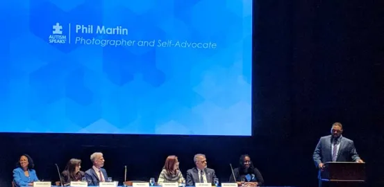 Phil Martin presenting at podium with panelists sitting at long table