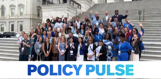 group of ~70 people standing on steps waving; white banner across the bottom with blue words of "POLICY PULSE"
