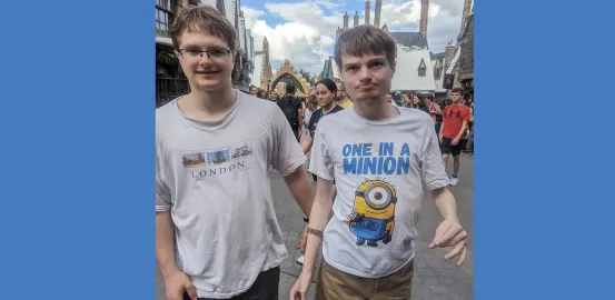 Two young men walk towards the camera at a thempark. One has a London tshirt on and one has Minion character shirt on