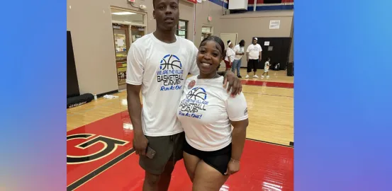 Two siblings stand on a basketball court in matching shirts 