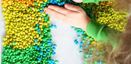 Sensory game with different colored beans on a table and a toddler touching them