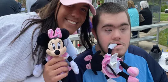 Smiling young woman in Minnie Mouse ears posing with a man in a blue jersey holding pink Minnie plush toys