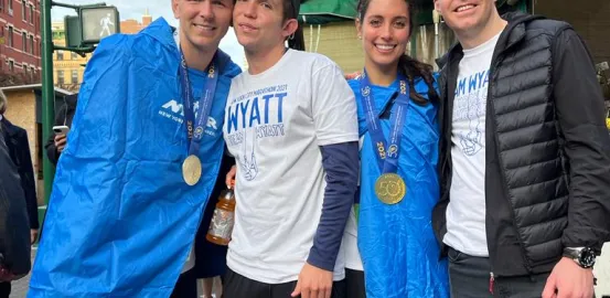 A man and a women in post marathon blue coats wear gold medals and smile with two other men in shirts that read Team Wyatt 