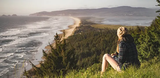 a woman sitting on a grassy hill over looking the ocean