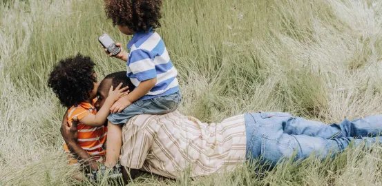 a father laying in a field with his 2 children hugging and sitting on top of him