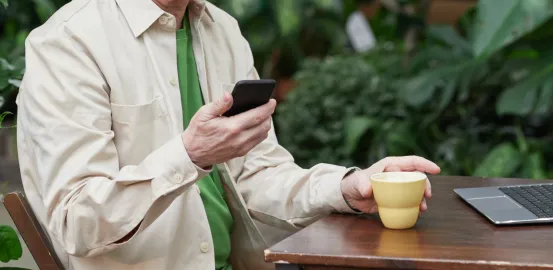 an older man sitting outside with a coffee and looking at his cell phone