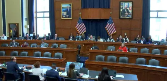 View of committee hearing room, looking at tiered rows of chairs with subcommittee members seated among them