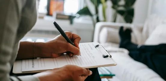 person sitting on a couch making a checklist on a clipboard