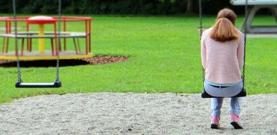 Girl sitting on a swing set alone in a park 