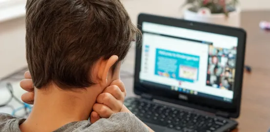 boy looking at laptop screen that shows a video conference presentation
