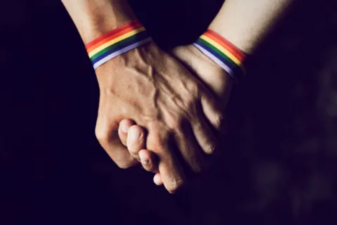 2 people holding hands with Pride bracelets on