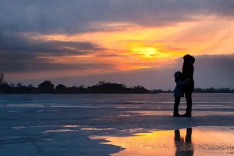 A mother and young child hugging on a beach at sunset