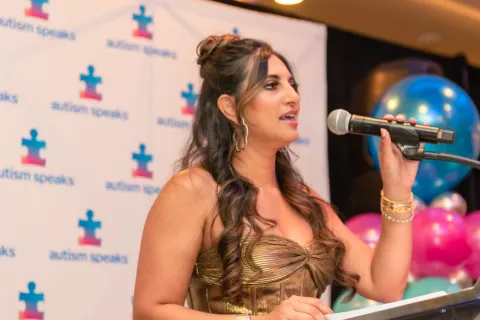 A woman wearing a gold dress speaking at an Autism Speaks event