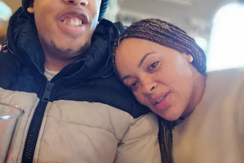 Close up of a woman with braided hair leaning her head on a young man shoulder while both wear winter coats