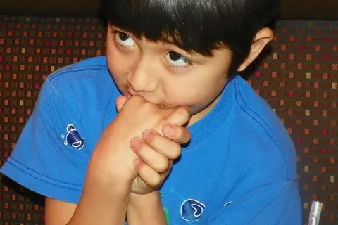 Autistic child in a blue shirt with their hands clasped