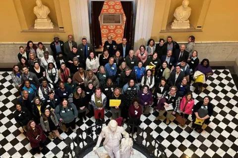Large group of advocates standing on a black and white checkered floor in the capitol atrium