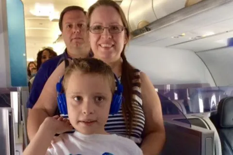 a boy and his mom and dad boarding a plane, the boy is wearing blue headphones
