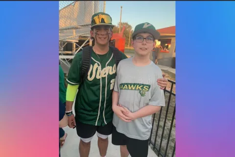 Two brothers stand side by side in green basebeball uniforms 