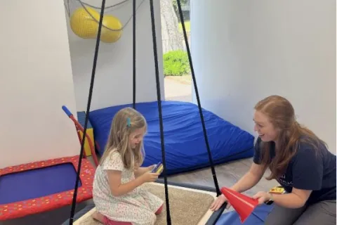 A young girl plays with her therapist on a blue mat 