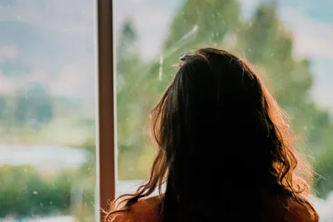 Woman looking at a lake and mountains out a window 