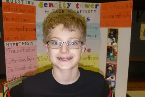 Zachary wearing a Star Wars shirt and standing in front of a school project with a smile