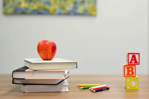 a stack of books, an apple on top, blocks and colored pencils on a desk