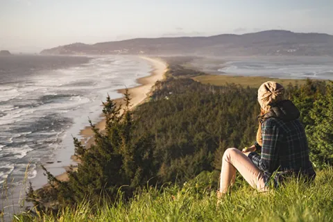 a woman sitting on a grassy hill over looking the ocean