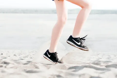 close up of someone exercising on sand beach wearing black sneakers