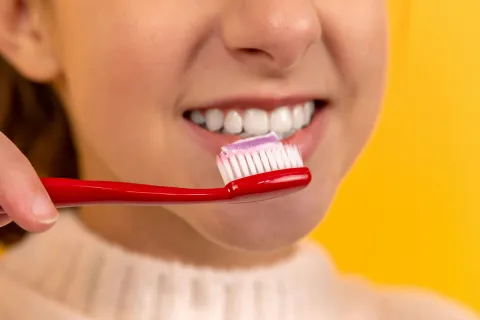 Kid brushing teeth with red toothbrush and purple toothpaste