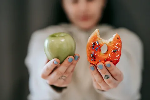 girl with nails painted blue holding up a donut in one hand and an apple in the other