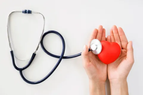 hands holding a red heart stress ball next to a stethoscope